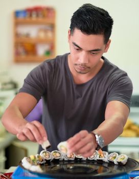 When it comes to sushi, hes a perfectionist. a young man arranging sushi on a platter at home.