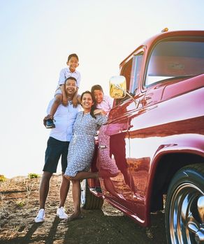 Taking the family on a road trip vacation. a cheerful family posing for a portrait together outside next to a red pickup truck.