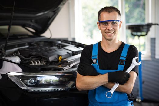Portrait of european caucasian car mechanic in uniform with tools in his hands looks at the camera and laughs happily. Car service concept