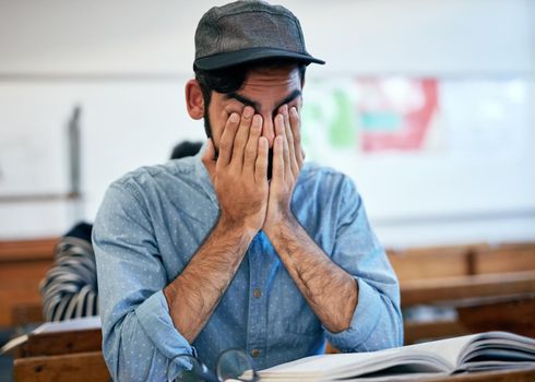 Studying all night has made him tired. an university student covering his face in exhaustion in class.