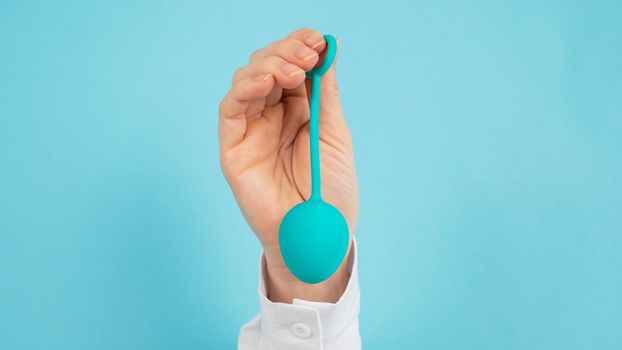 A woman's hand sticks out of a hole in a blue background and holds a vaginal egg.