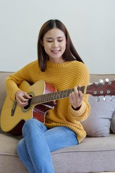 woman playing guitar on sofa happily in the house