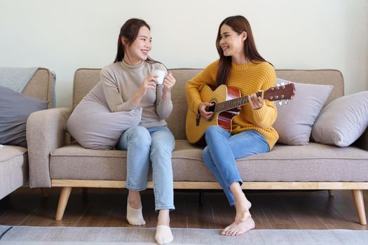 LGBTQ, female couple playing guitar happily on the sofa in the house.
