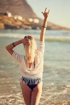 Keep your spirit salty. Rearview shot of a young woman on the beach with her hand in the air.