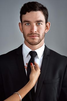 Nothing tempts like a man in a well tailored suit. Studio portrait of a handsome young businessman being touched by an unrecognizable womans hand against a gray background.