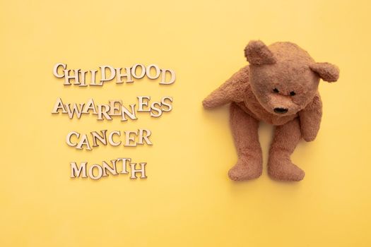 Childhood cancer awareness month text from wooden letters and teddy bear on yellow background