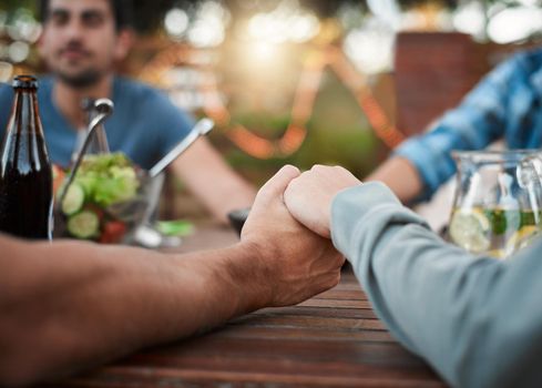 Everyone hold hands and close your eyes. two unrecognizable people holding hands around a table outside in a garden.