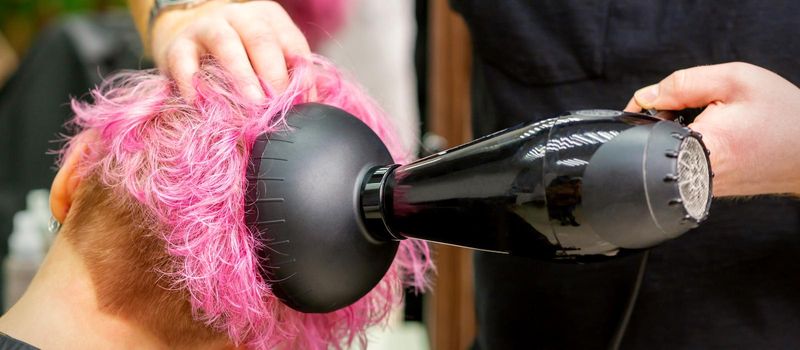 Hairdresser drying pink hair of client