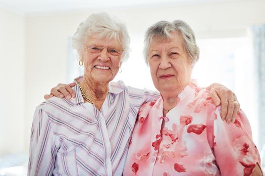 Time together means so much to us. Portrait of two happy elderly women embracing each other at home.