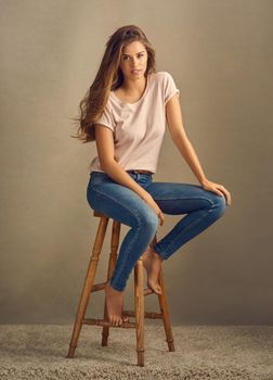 You have what it takes. Studio shot of a beautiful young woman sitting on a stool against a plain background.