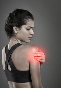 No pain no gain. Studio shot of a young attractive woman holding her injured shoulder that gets shown through CGI.