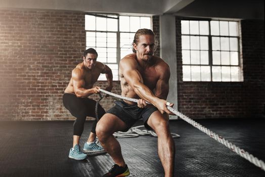 Youre getting stronger with every second. two muscular young men pulling on a rope in a gym.