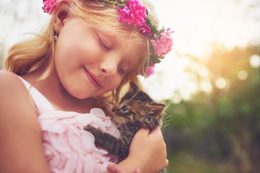 My furry friend. a happy little girl holding a kitten and smiling while sitting outside in nature.