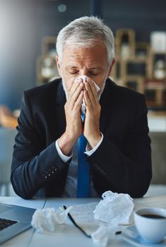 I hope this doesnt get worse. a frustrated businessman using a tissue to sneeze in while being seated in the office.