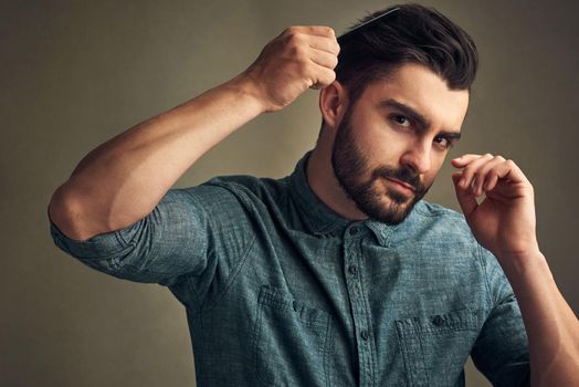 Beard season is here. Studio shot of a handsome young man combing his hair against a grey background.