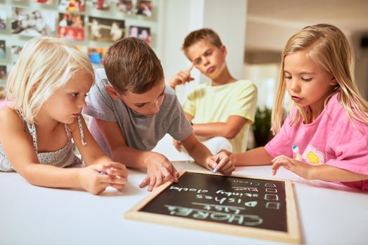Doing chores teaches kids to take responsibility. kids writing a list of chores on a chalkboard at home.