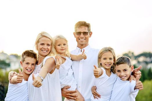 Thumbs up if you love your family. a happy family with their thumbs up outdoors.