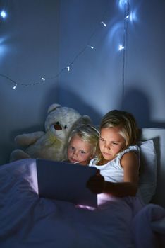 Learning and growing through the digital age. two little girls using a digital tablet before bedtime.