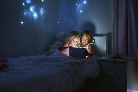 Taking turns playing their favourite games online. two little girls using a digital tablet before bedtime.