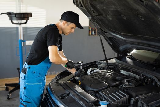 Empowering male mechanic is working in car service. Man is working on an usual car maintenance. He's using ratchet. Car mechanic using wrench to repair the engine, car service. Auto service