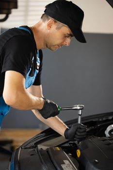 Car mechanic using wrench to repair the engine, car service. Auto service. Empowering male mechanic is working in car service. Man is working on an usual car maintenance. He's using ratchet