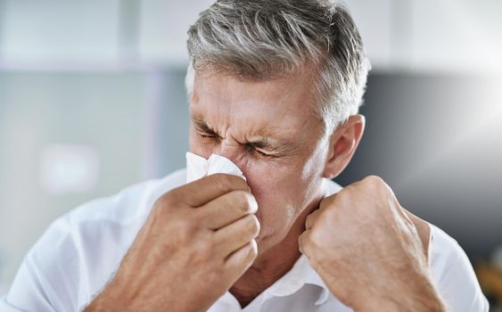 Allergies are not fun. a mature businessman blowing his nose in the office.