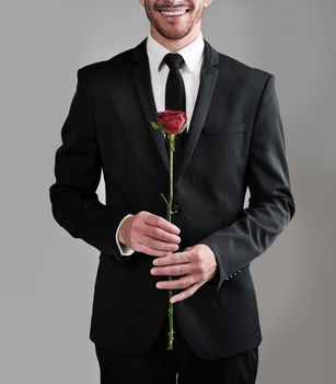 The perfect gentlemen attire. Studio shot of a well-dressed man holding a red rose against a gray background.