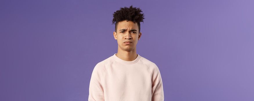 Close-up portrait of skeptical and gloomy, disappointed hispanic young man frowning upset, feel uneasy about bad idea, grimacing with disapproval, standing unhappy purple background