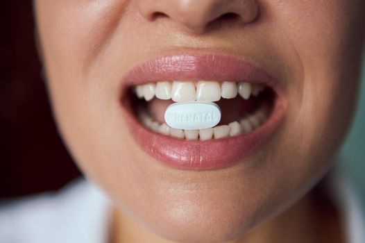 White pill with dietary supplement in the mouth of blurry pregnant woman, smiling beautiful toothy smile. Prenatal care