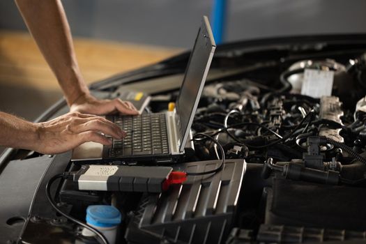 Auto mechanic uses laptop while conducting diagnostics test. Modern car service. Computer diagnostics of the car. European car mechanic holds a digital device