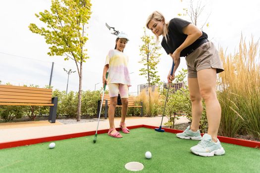 Detail of young woman and daughter playing mini adventure golf on a beautiful sunny summer day.
