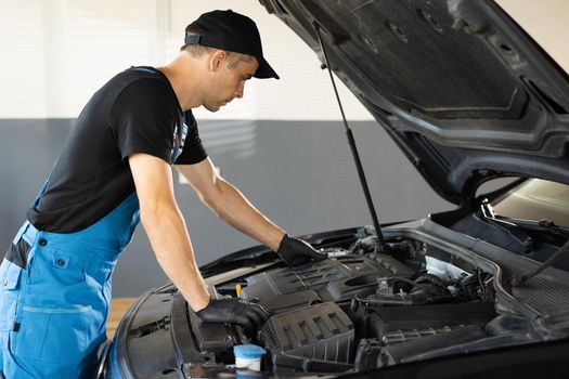 Mechanic man open a car hood and check up the engine. Car mechanic noting repair parts during open car hood engine repair at garage. Overheating of a car engine. Motor with open hood