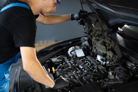 Car mechanic noting repair parts during open car hood engine repair at garage. Unrecognizable mechanic man open a car hood and check up the engine. Overheating of a car engine. Motor with open hood