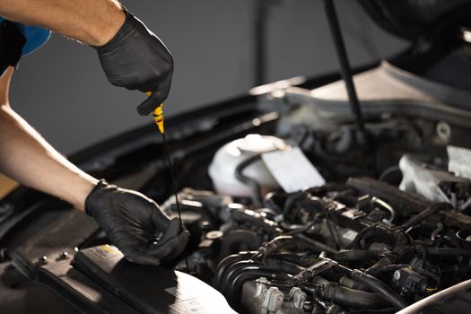 Close-up of automotive mechanic checks the oil level on the car engine dipstick. Car oil quality. Inspection of the engine and checking motor oil level. Man checks the car oil level with dipstick