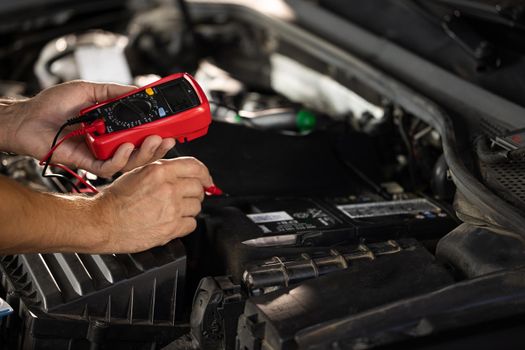 Mechanic doing car inspection, he is testing car battery with tester. Check battery voltage with electric multimeter. Man using multimeter to measure the voltage of the batteries