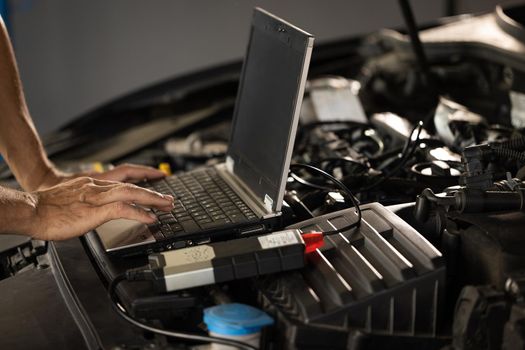 Computer diagnostics of the car. European car mechanic holds a digital device. Auto mechanic uses laptop while conducting diagnostics test. Modern car service