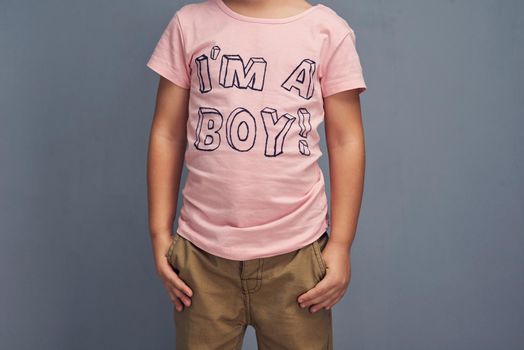 Pink is a color, not a gender. Studio shot of a boy wearing a t shirt with Im a boy printed on it against a gray background.