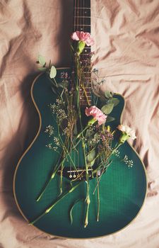 Music makes your thoughts grow. High angle shot of a green guitar lying on a bed with flowers arranged on it.