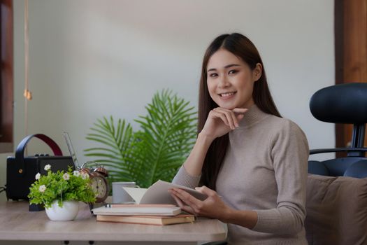 Beautiful Asian Woman reading a book at her desk at home