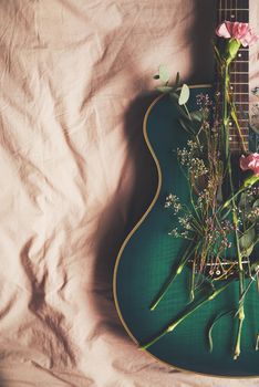 Green guitar fingers. High angle shot of a green guitar lying on a bed with flowers arranged on it.