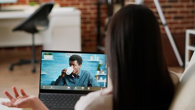 Young adult woman talking to coworker on laptop virtual videocall meeting while working remotely