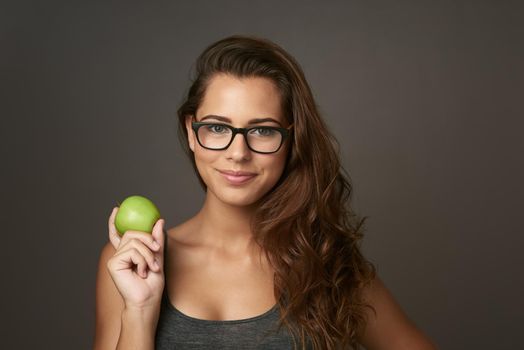 My healthy diet helps my hair be healthy too. Studio shot of a beautiful young woman holding an apple against a brown background.