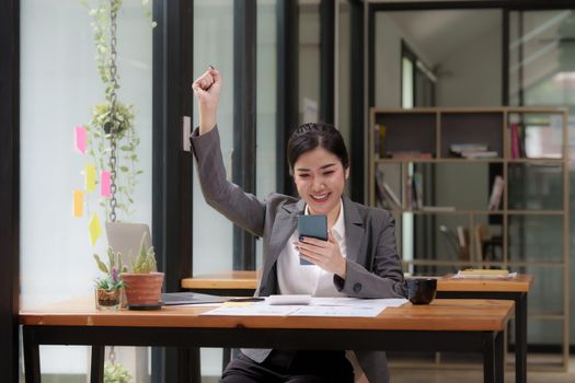 Happy Asian man using smartphone while have a good news working at office