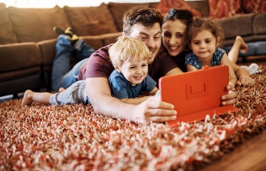 Theres something online for all ages. a happy young family looking at a tablet together while lying on the carpet in their lounge.