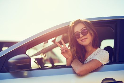 Finding a little peace and quiet. Portrait of a young woman giving you the peace sign while sitting in her car.