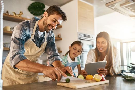 There are so many exciting recipes to try online. two happy parents and their young daughter trying a new recipe in the kitchen together.