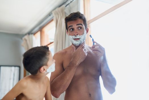 Go against the grain. a handsome young man teaching his son how to shave in the bathroom.
