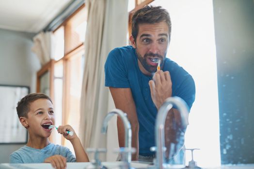 Make sure you get those teeth at the back. a handsome young man and his son brushing their teeth in the bathroom.