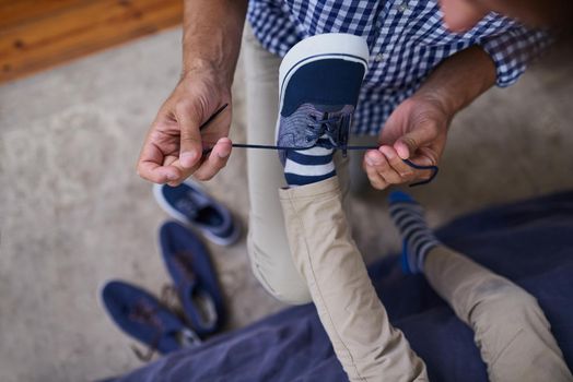 Helping him with his laces. High angle shot of an unrecognizable man tying his sons shoelaces at home.