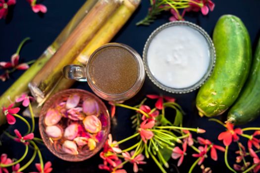 Diy face mask for youthful skin on a black wooden board consisting of some sugarcane juice, cucumber, rose water, and fresh cream. Shot of sugarcane juice, raw cucumber, and cream with rose water.